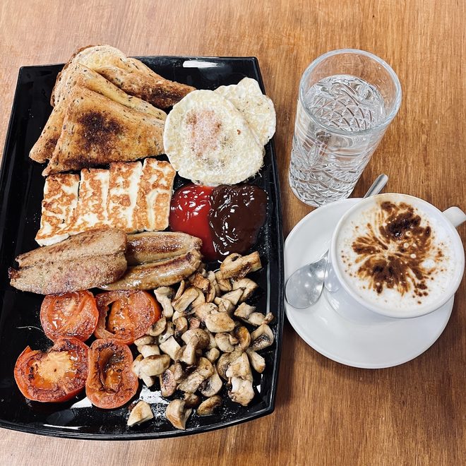 A mixed grill breakfast platter on a black tray with a cappuccino alongside.