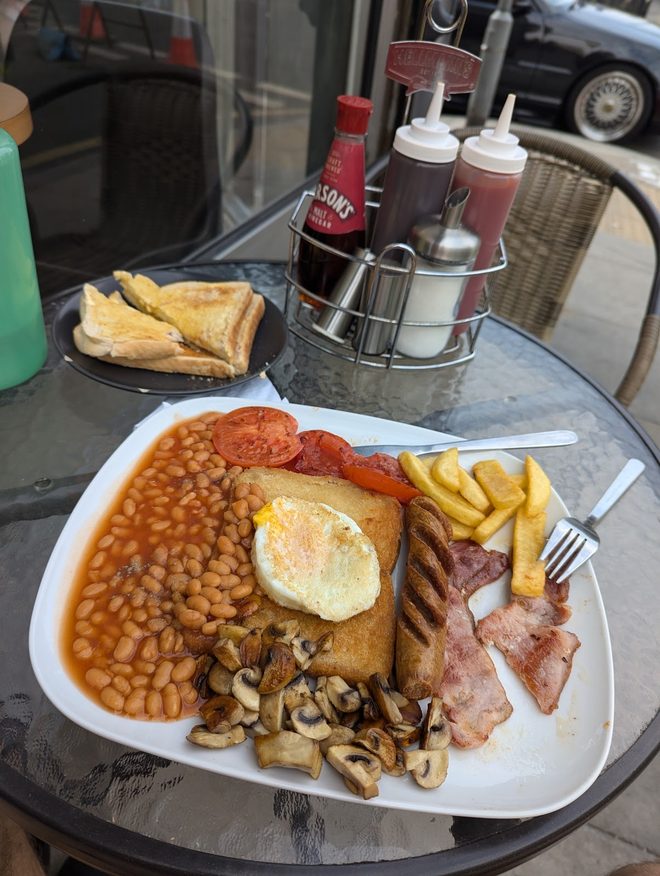 A breakfast plate with chips and beans on an outdoor metal table with sauce bottles.
