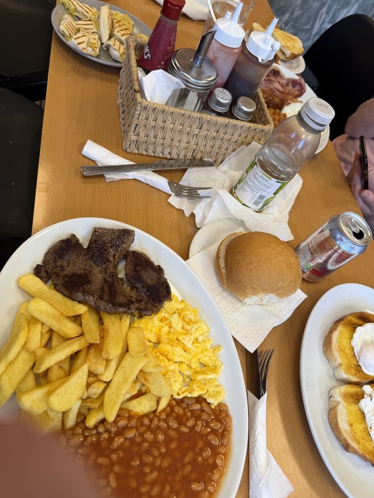 A table set with steak, chips, scrambled egg and beans, a bread roll, drinks and a condiment basket.